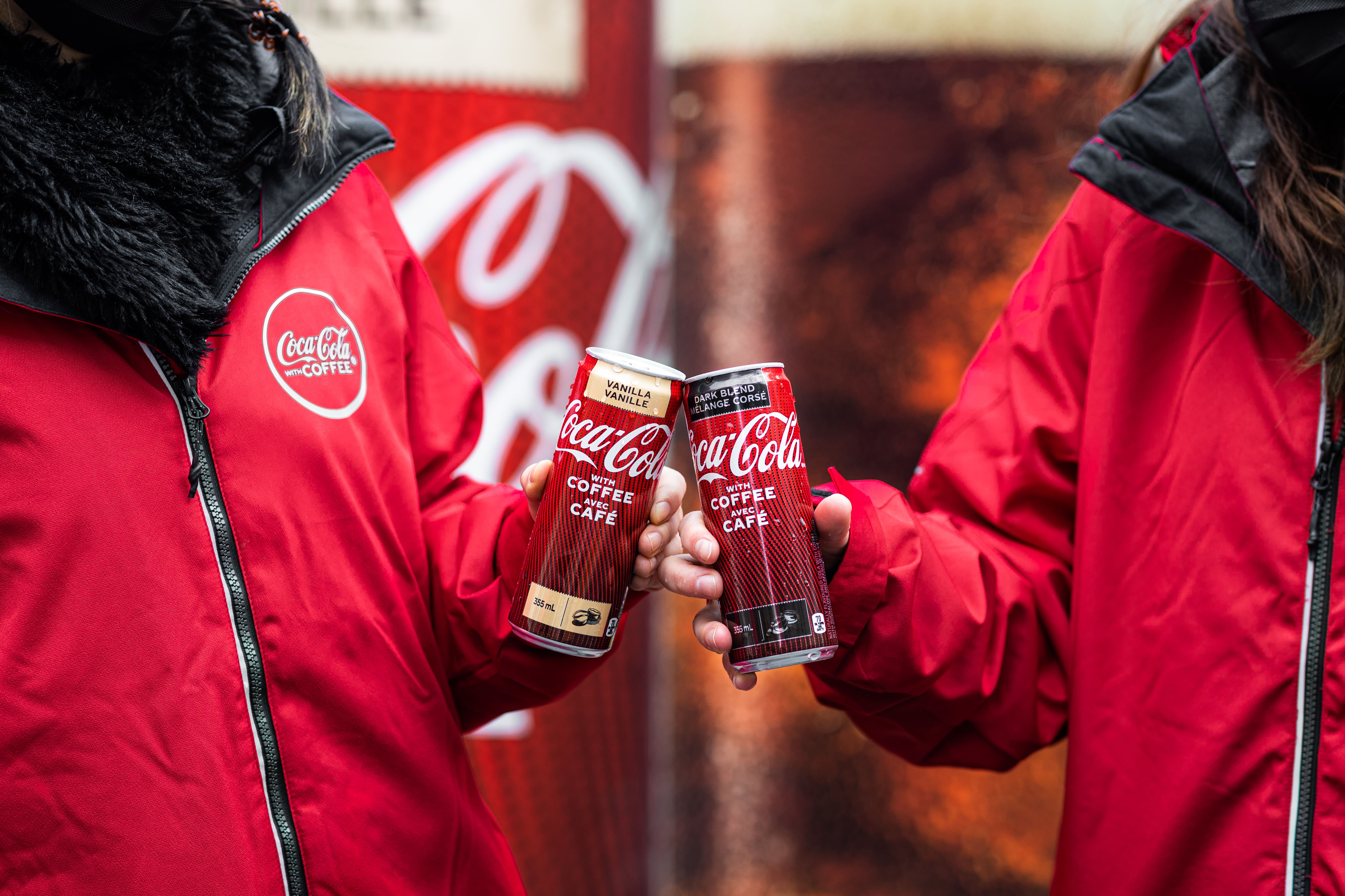 Two people with cans of Coke tapping each other's cans